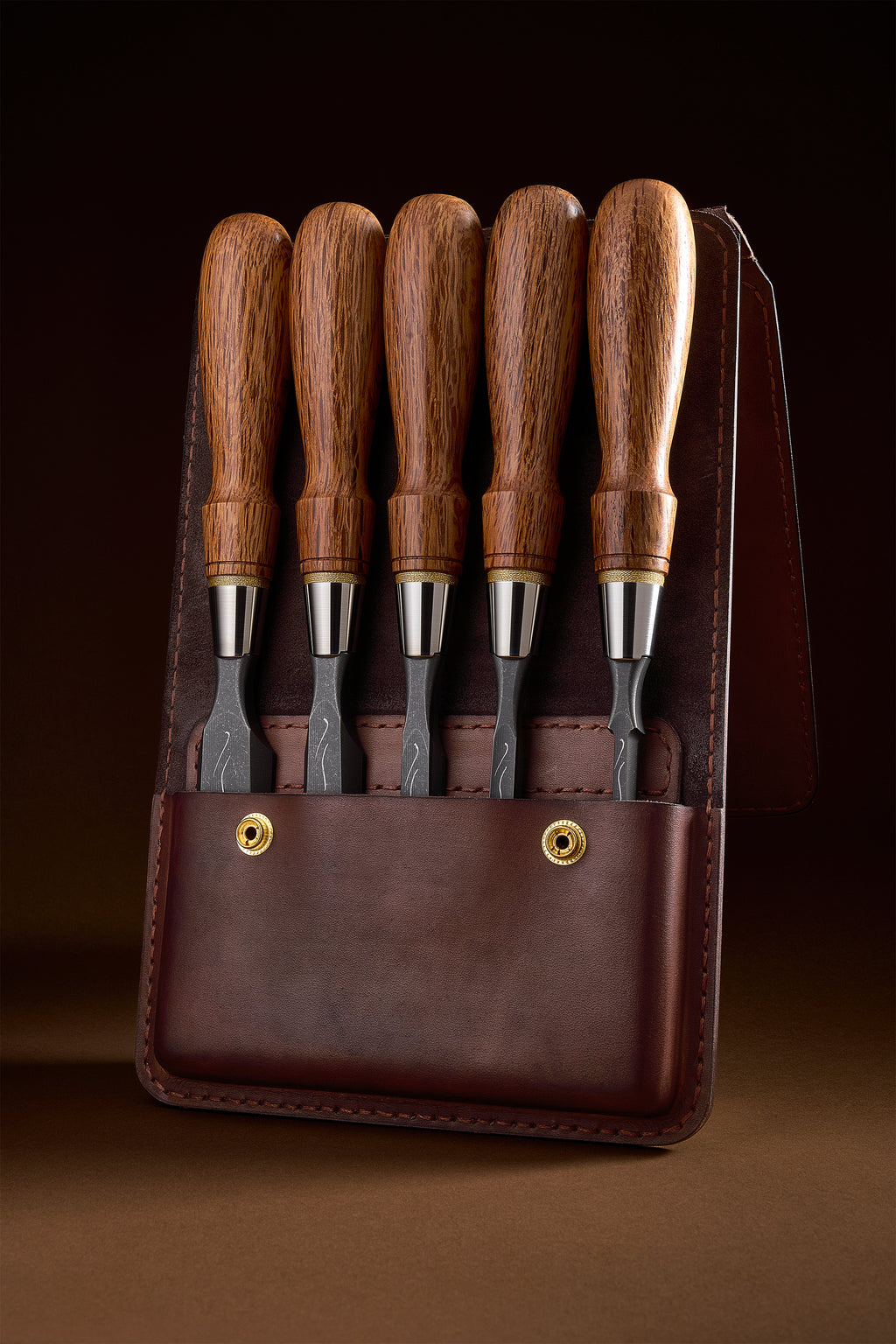 Full set of five X-2 chisels standing handles-up in the brown leather pouch against a dark background