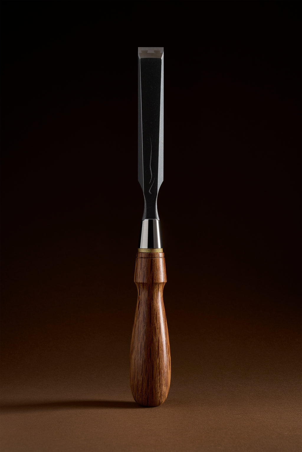 Wide X-2 bench chisel upright: black titanium body, polished steel face, red bamboo-leaf oak handle with brass collar