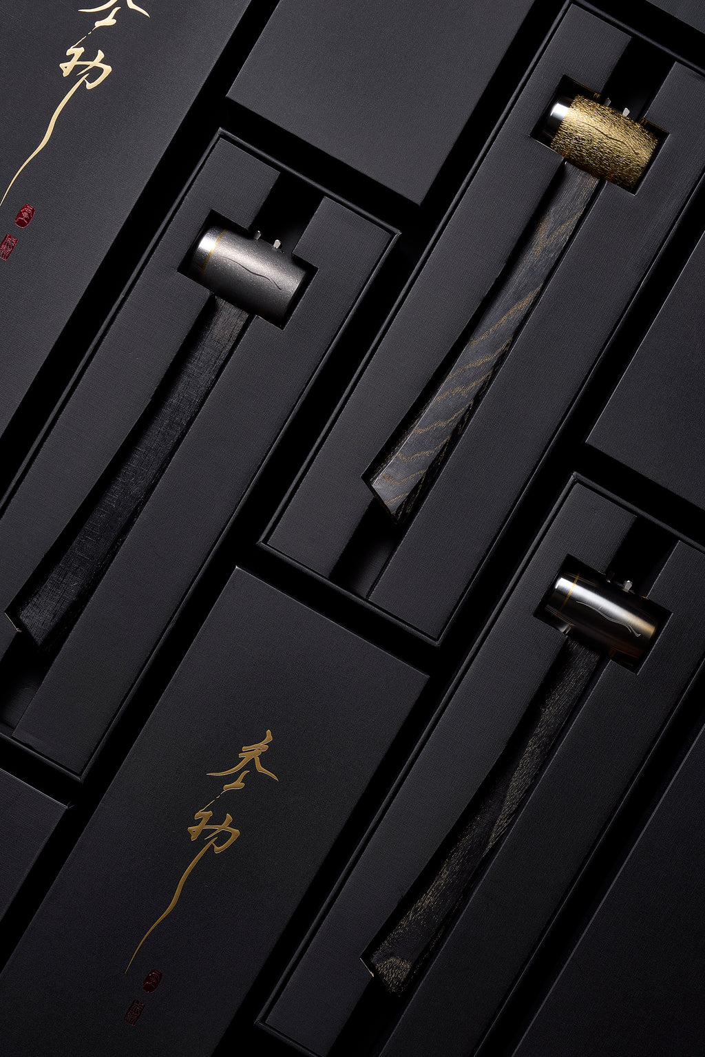 Three F-4 hammers seated in black presentation boxes with gold calligraphy: brushed titanium and hand-carved brass heads, dyed hickory handles