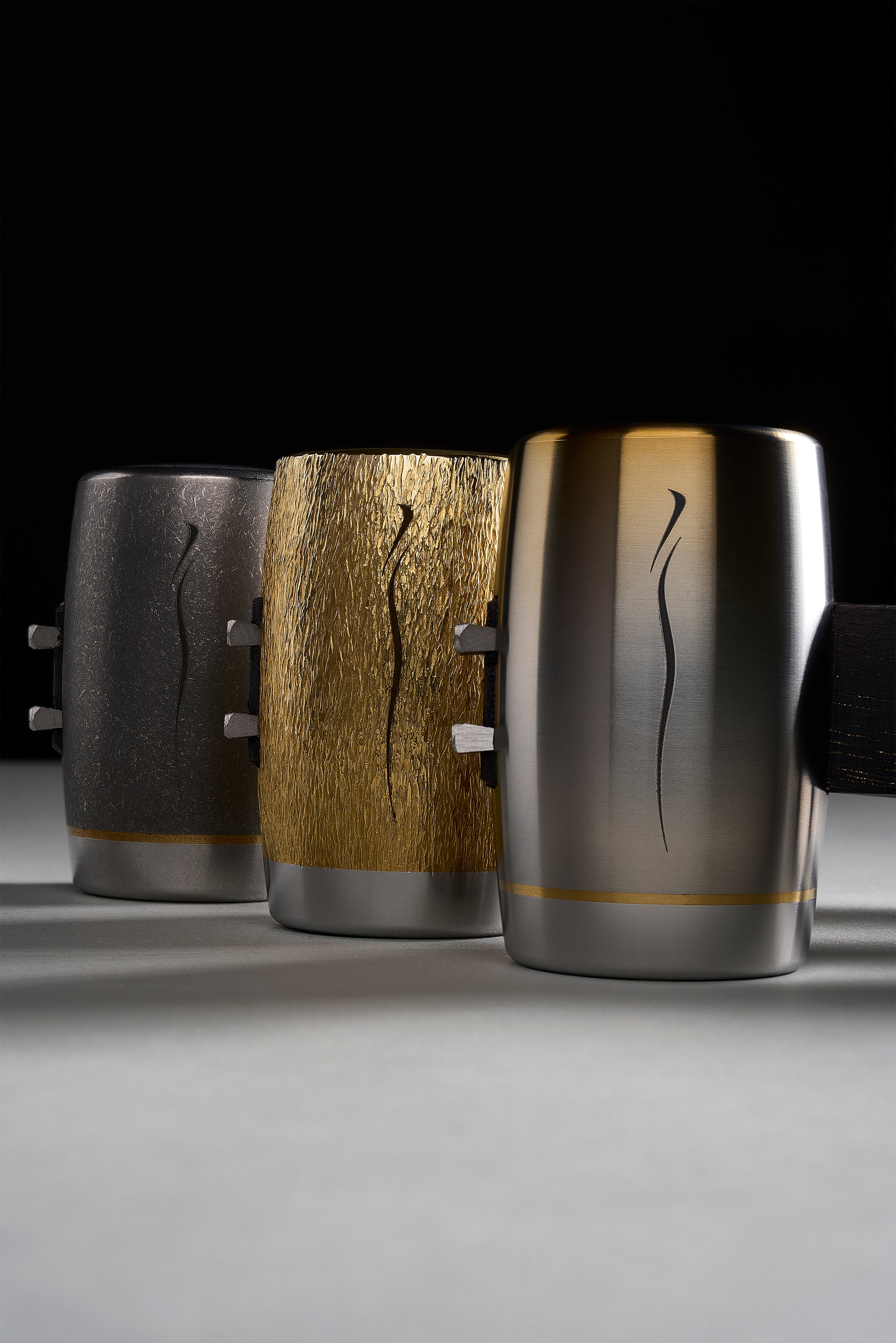 Three F-4 heads side by side: flame-anodized titanium, hand-carved brass, brushed titanium with engraved line