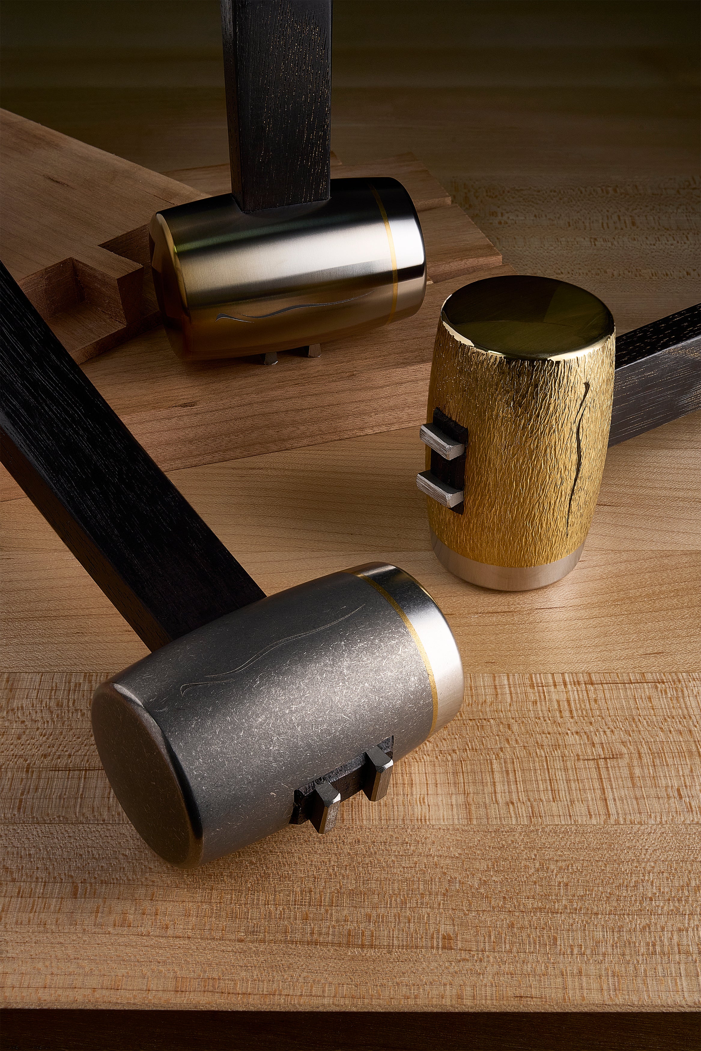 Three F-4 hammers on a maple bench: brushed titanium, hand-carved brass, and flame-anodized heads
