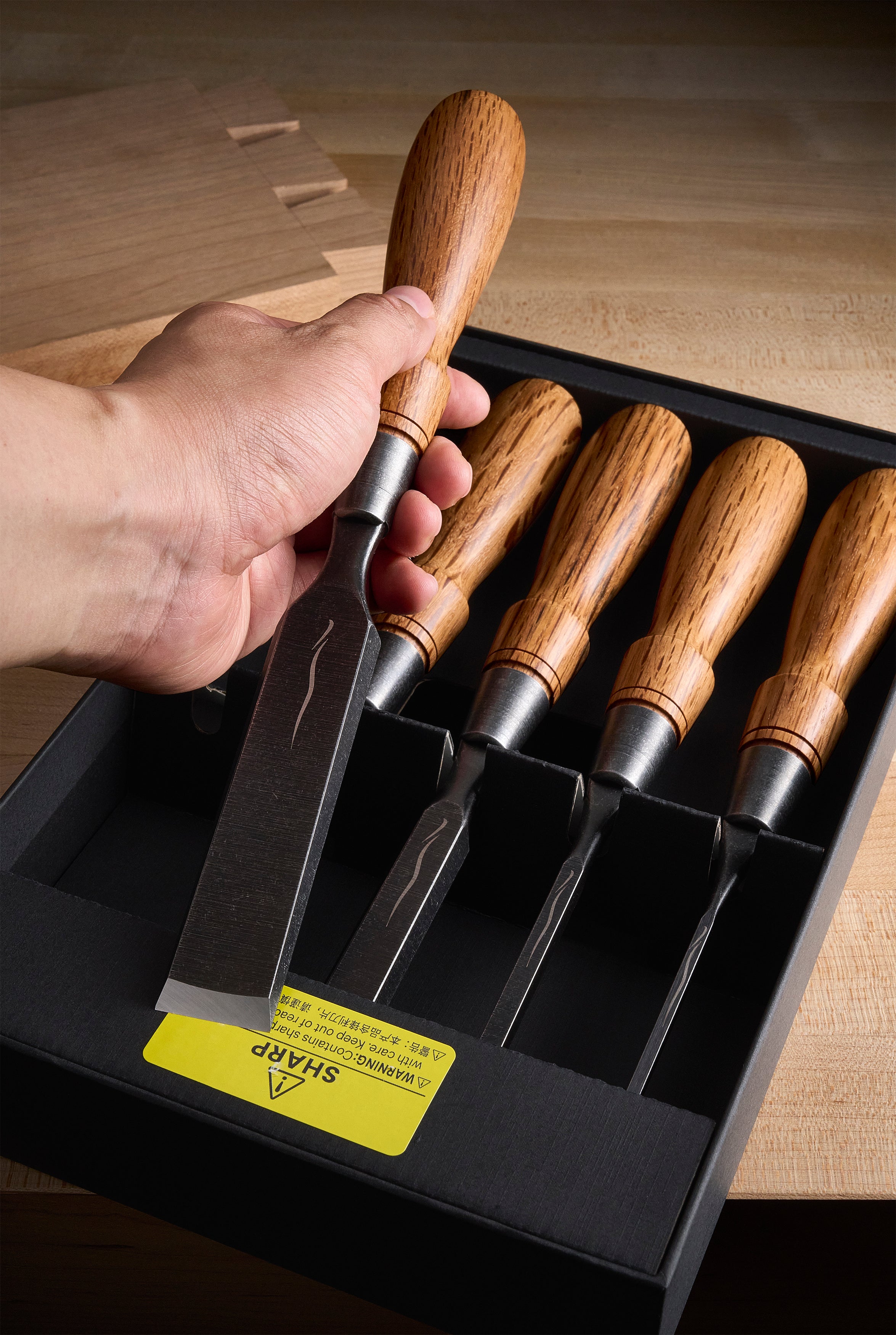 A hand lifts the widest chisel from a boxed Y-2 set at the workbench