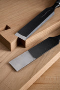 Two Y-2 bench chisels on a workbench, one seated in a chopped recess, polished bevels against dark blade backs
