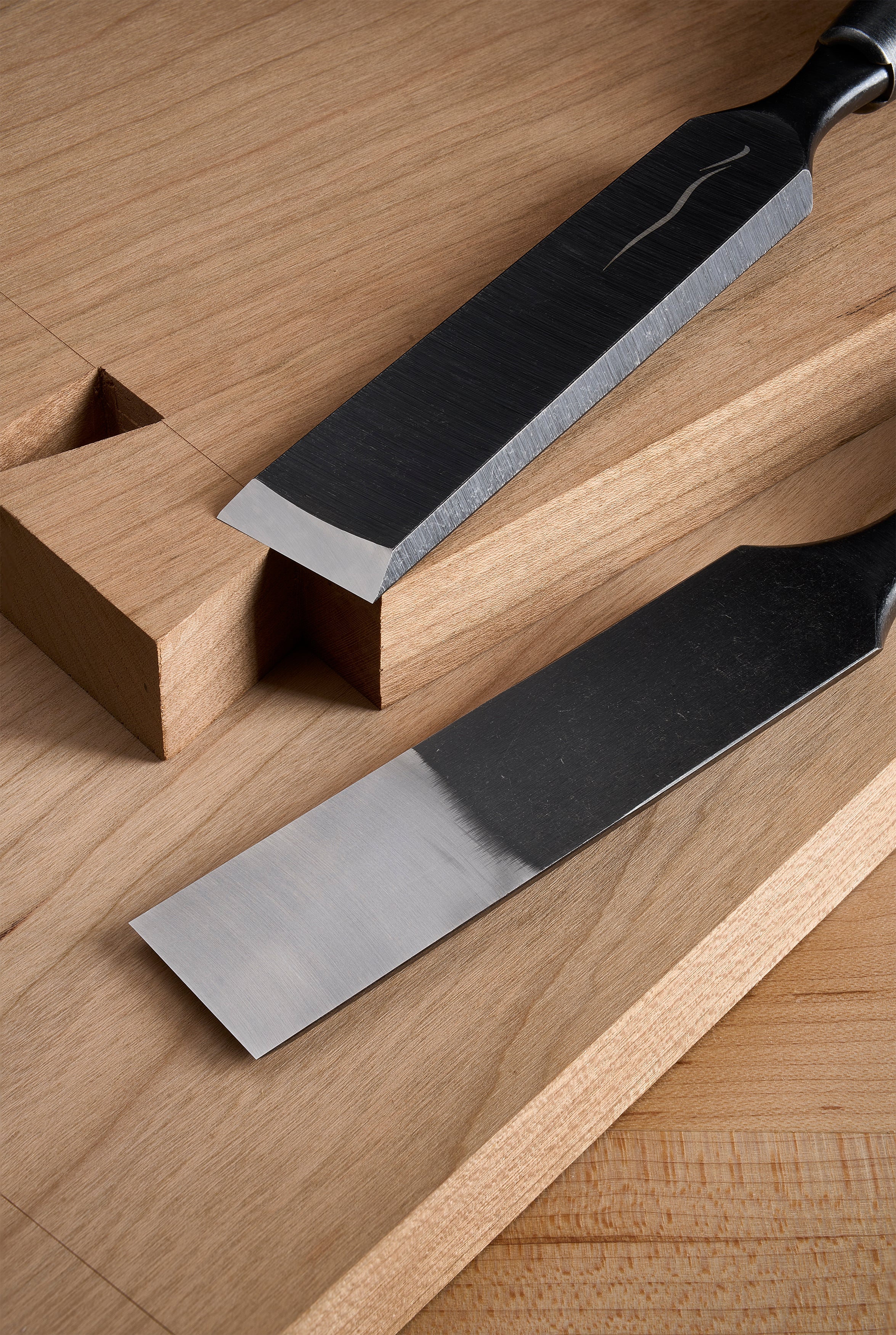 Two Y-2 bench chisels on a workbench, one seated in a chopped recess, polished bevels against dark blade backs