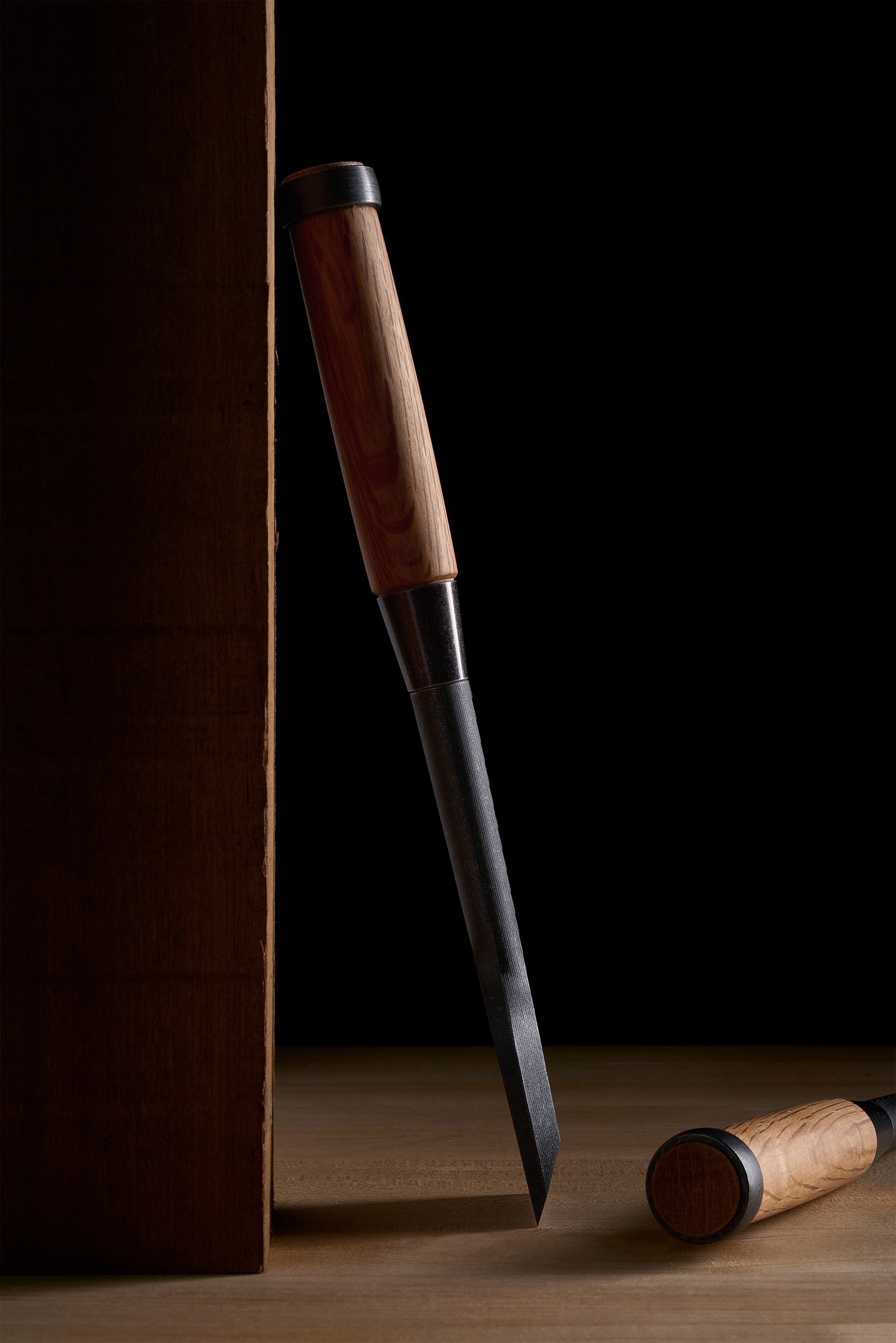 Narrow TB-1 chisel standing against a board, iron ferrule below the wooden handle
