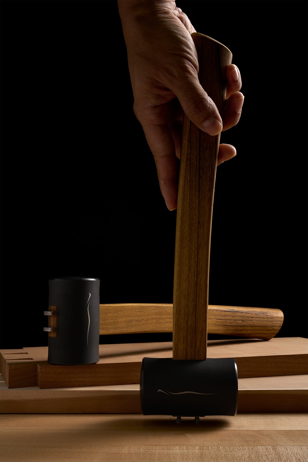A hand holding a Zen-Wu F-3 hammer upright on the bench, a second F-3 lying behind it